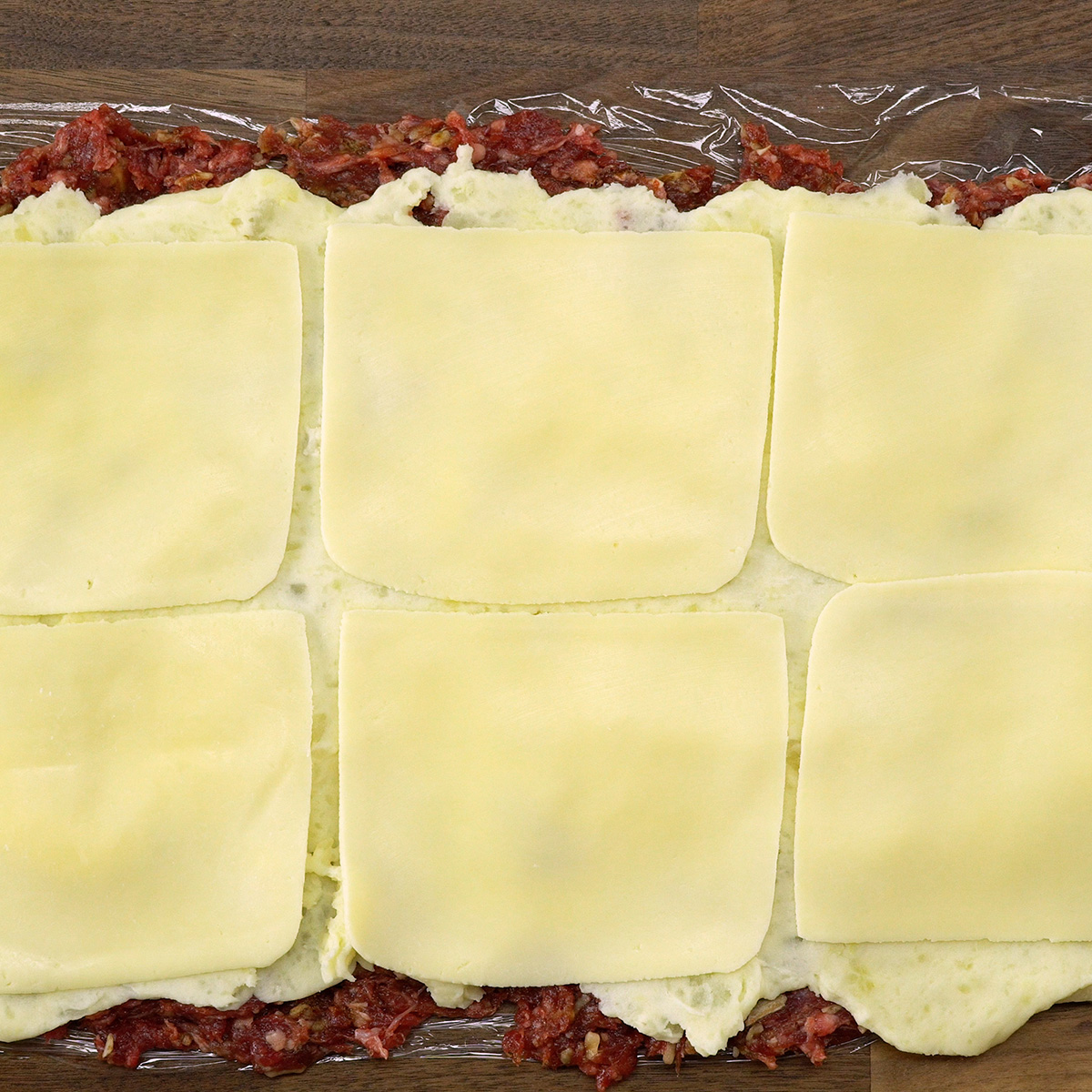 Purê de batata e mussarela distribuídos sobre a carne para montagem do rolo.