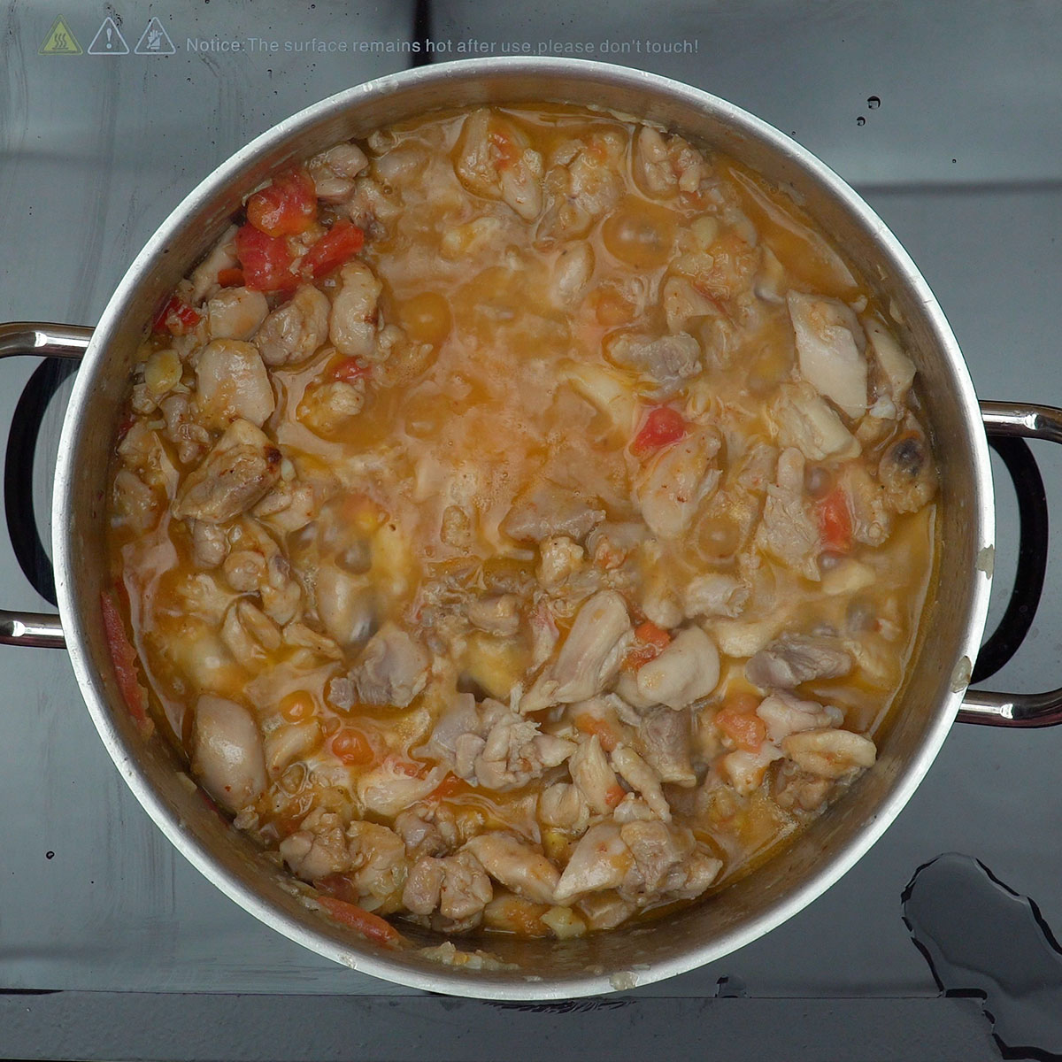 Frango cozinhando lentamente no caldo temperado com tomate e cebola.