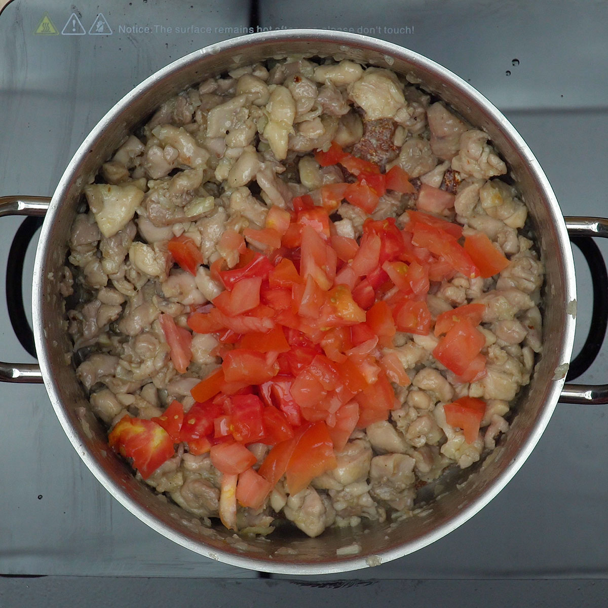 Cebola, alho e tomate refogando junto ao frango dourado na panela.
